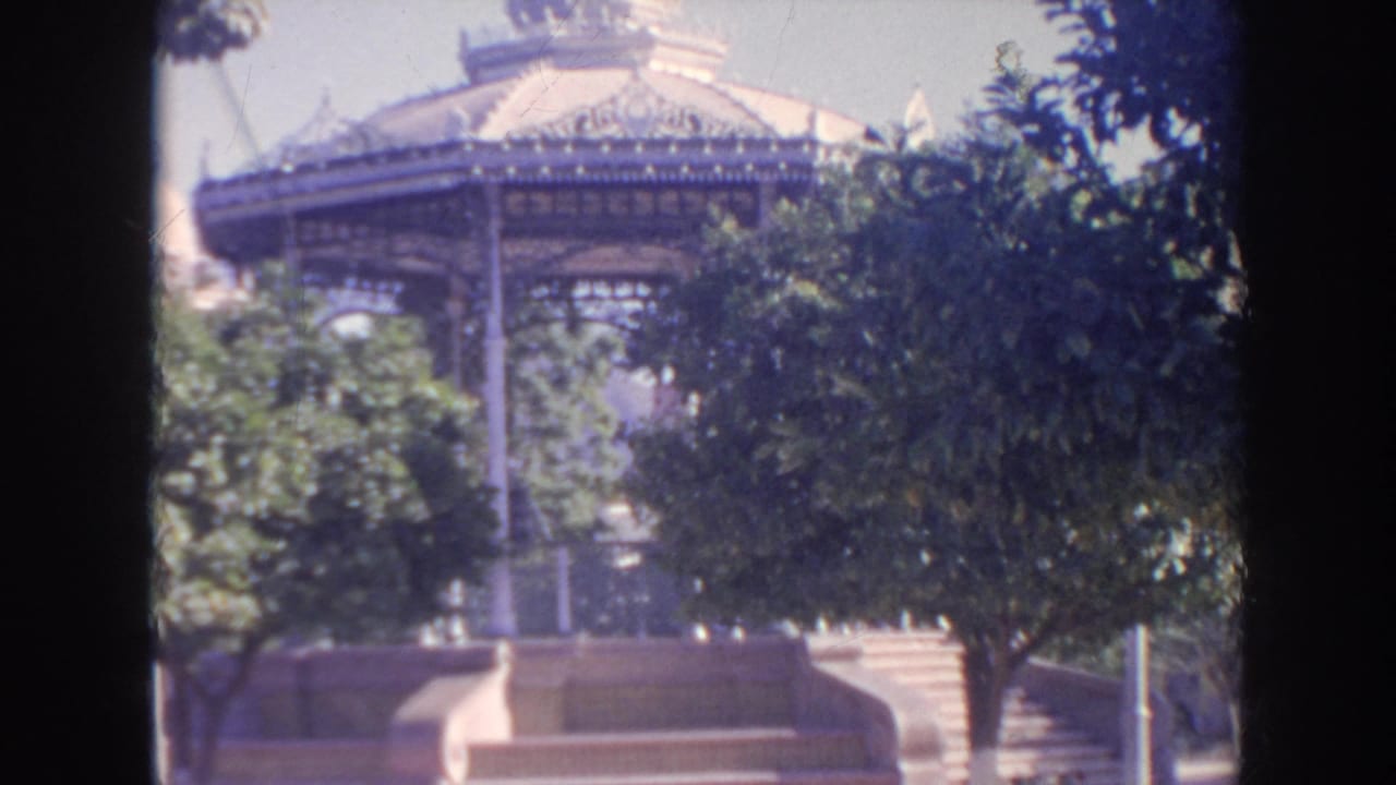 1961 8mm travel footage shows an ornate outdoor pavilion behind trees, steps, and dark vertical edge shadows.