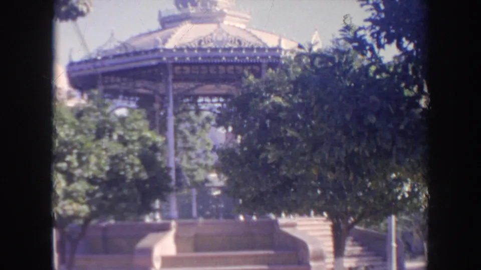 1961 8mm travel footage shows an ornate outdoor pavilion behind trees, steps, and dark vertical edge shadows.