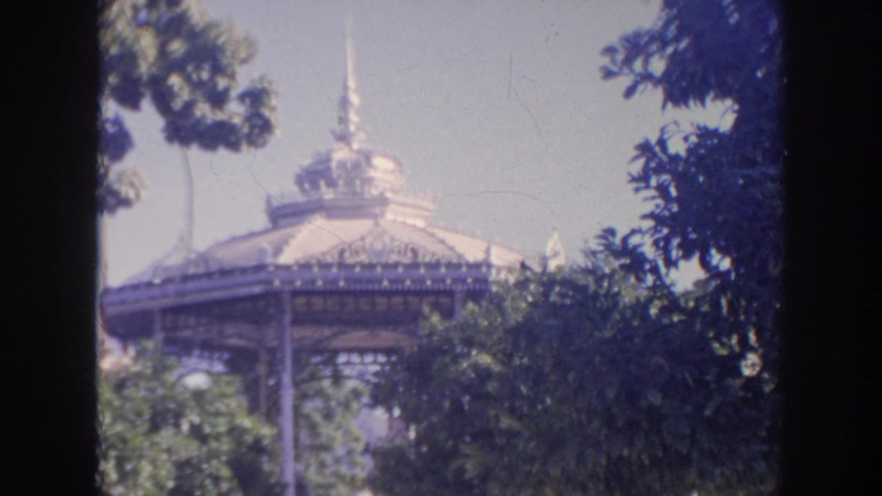 A second 8mm frame holds on the ornate pavilion roof, leafy trees, and steps in a bright outdoor travel setting.