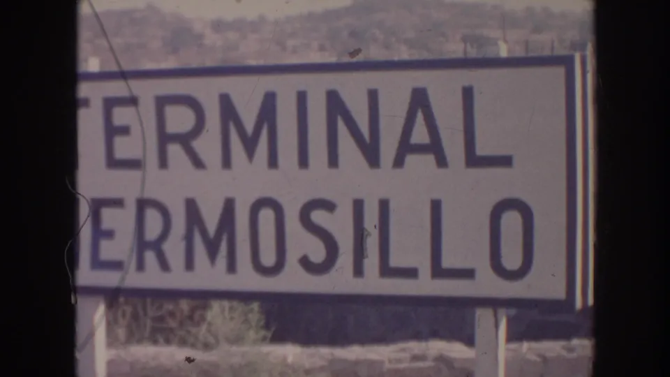 1961 8mm frame showing a close view of a Terminal Hermosillo sign with dry hills behind it.
