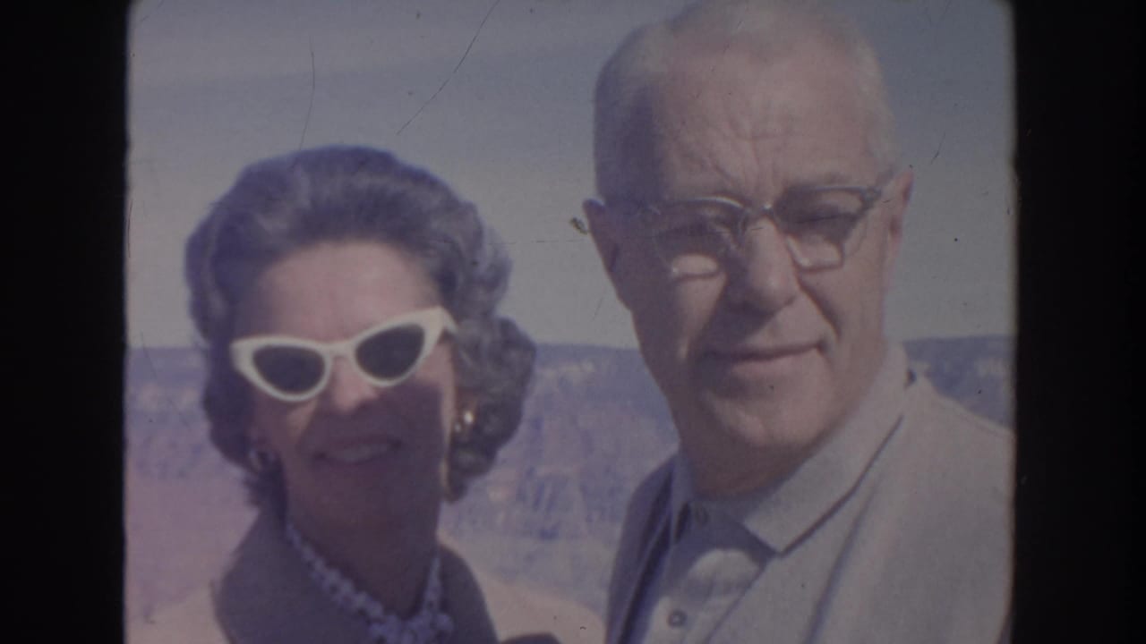 Older woman in white cat-eye sunglasses poses beside an older man in glasses at a canyon overlook.