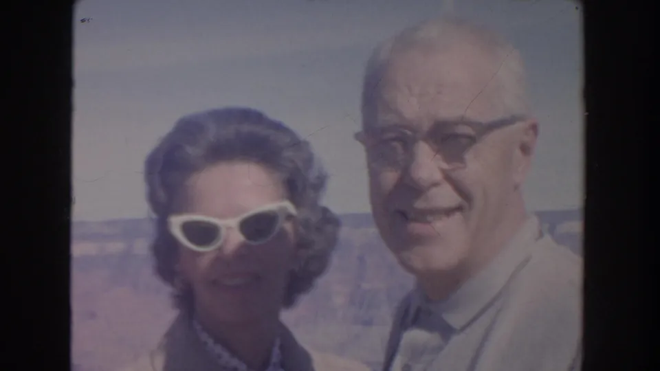 1962 home-movie close-up of an older couple smiling at a scenic Arizona canyon overlook in bright daylight.