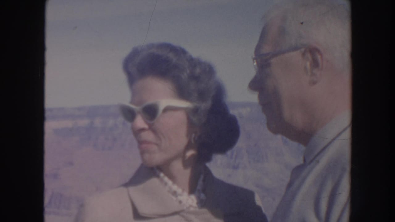 Woman in white cat-eye sunglasses faces an older man at a canyon overlook.
