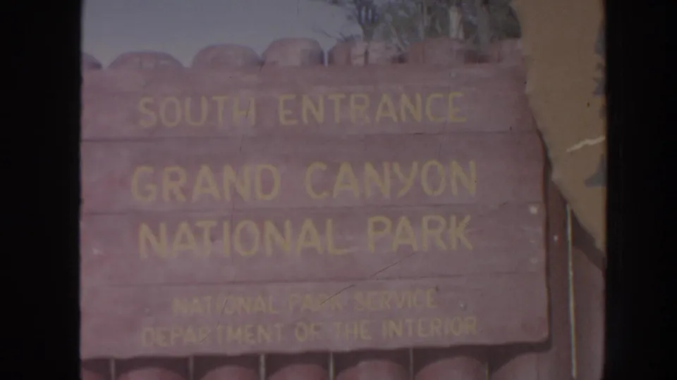 Faded 8mm frame of the Grand Canyon National Park South Entrance sign, with yellow lettering and visible home-movie wear.