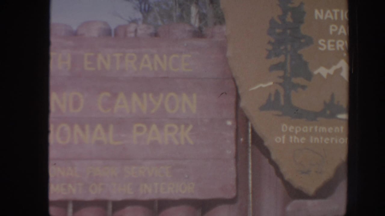 Weathered wooden entrance sign reading Canyon National Park, partly obscured by a National Park Service arrowhead emblem.