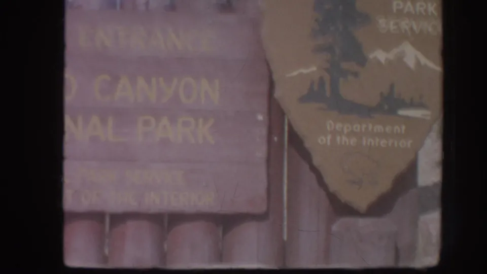 Faded 8mm frame of a Canyon National Park entrance sign with a National Park Service arrowhead sign at the right edge.