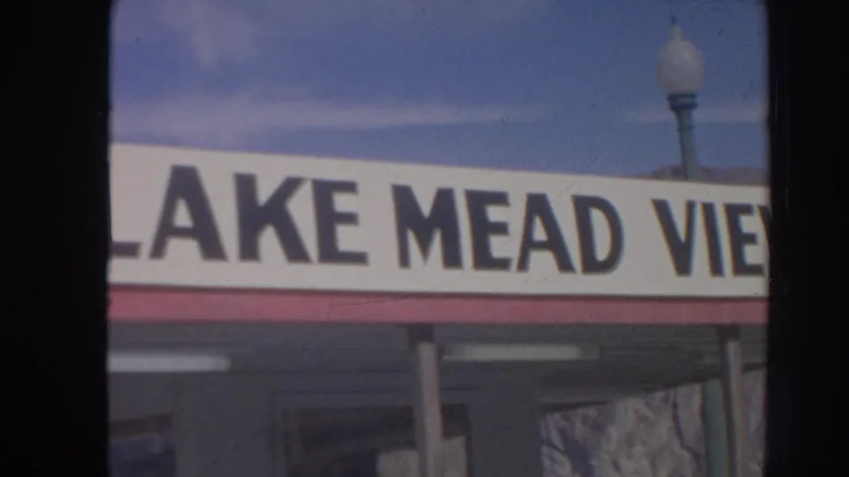 1962 8mm frame of a cropped Lake Mead View storefront sign with a globe streetlamp and blue sky above it.
