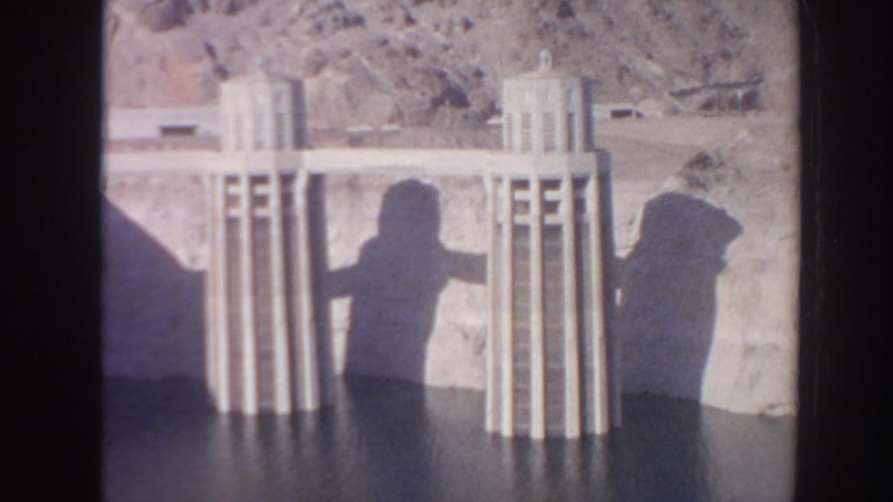 Concrete dam towers and long human shadows falling across reservoir water.