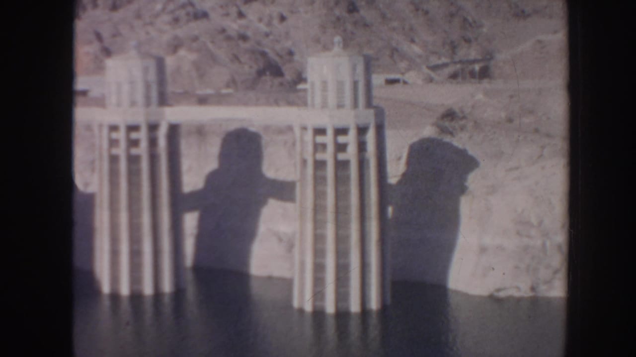 Dam towers beside water with dark visitor shadows on the concrete surface.