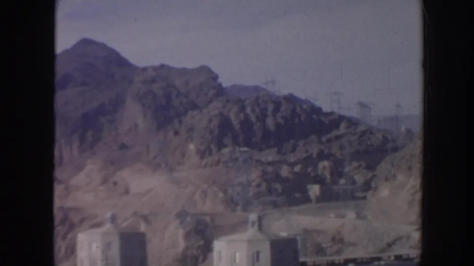 1962 Arizona 8mm view of rugged mountains, reservoir water, and partial concrete dam structures in a soft handheld frame.