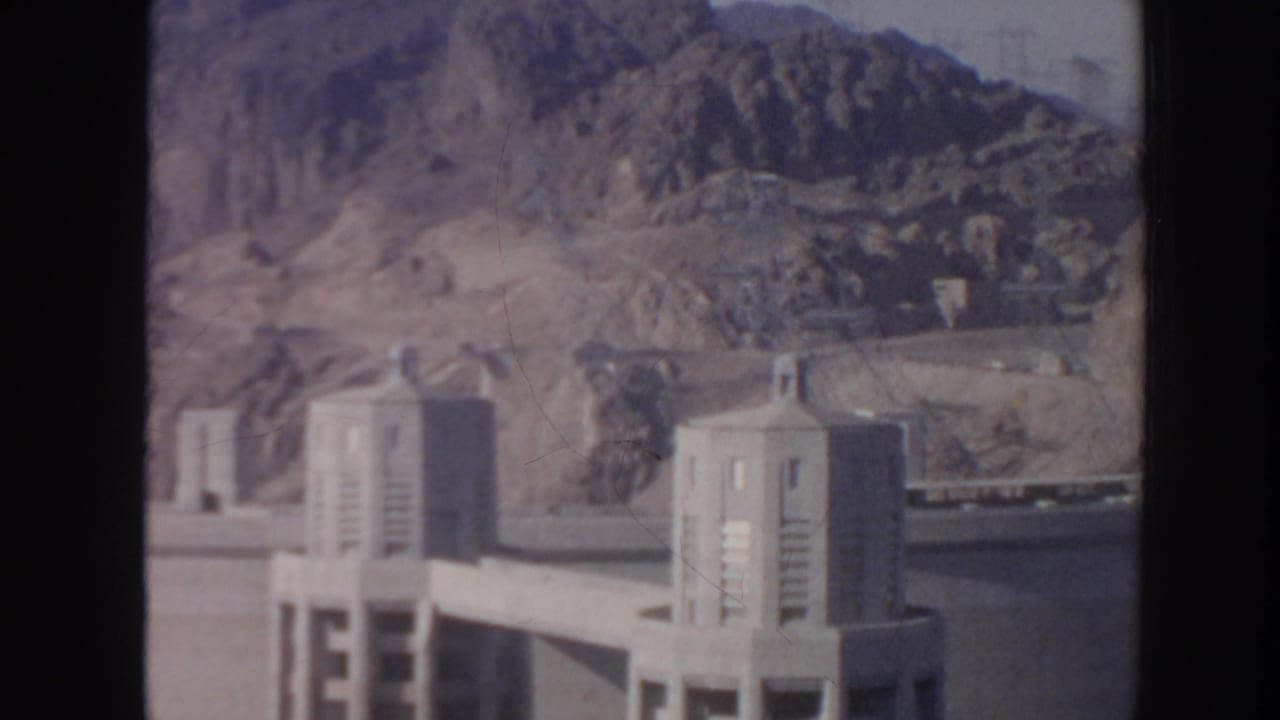 1962 Arizona 8mm frame showing Hoover Dam concrete towers against rugged desert mountains.