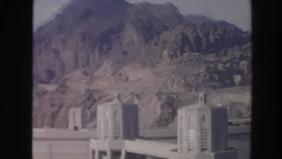 Hoover Dam towers and arid mountain ridges appear in a soft 1962 home-movie frame.