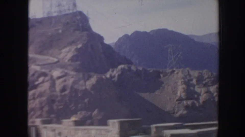 1962 Arizona view of rocky slopes near Hoover Dam with a road and power transmission structures.