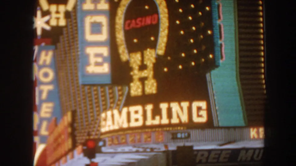 1962 8mm frame of Las Vegas neon signage, including a large gambling sign, hotel lettering, casino oval, and marquee bulbs.