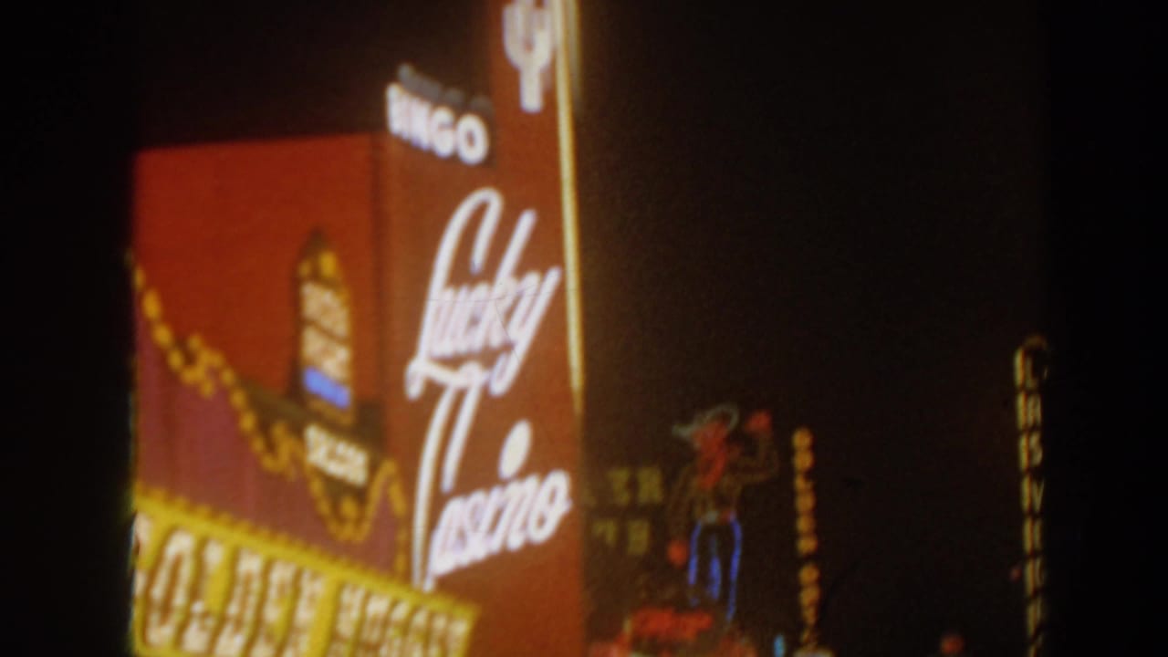 Nighttime 8mm view of Lucky Casino script signage beside a Golden Nugget marquee, with warm neon and bulb light.