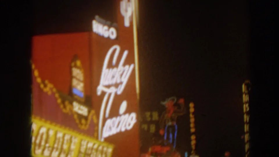 Nighttime 8mm view of Lucky Casino script signage beside a Golden Nugget marquee, with warm neon and bulb light.