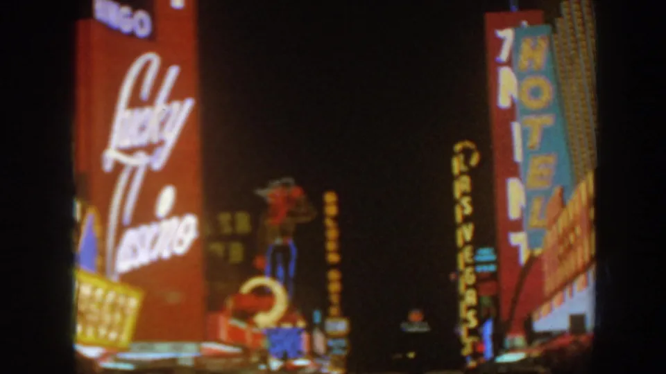 1962 home-movie frame showing Lucky Casino signage, a vertical motel sign, and distant casino lights in Arizona at night.