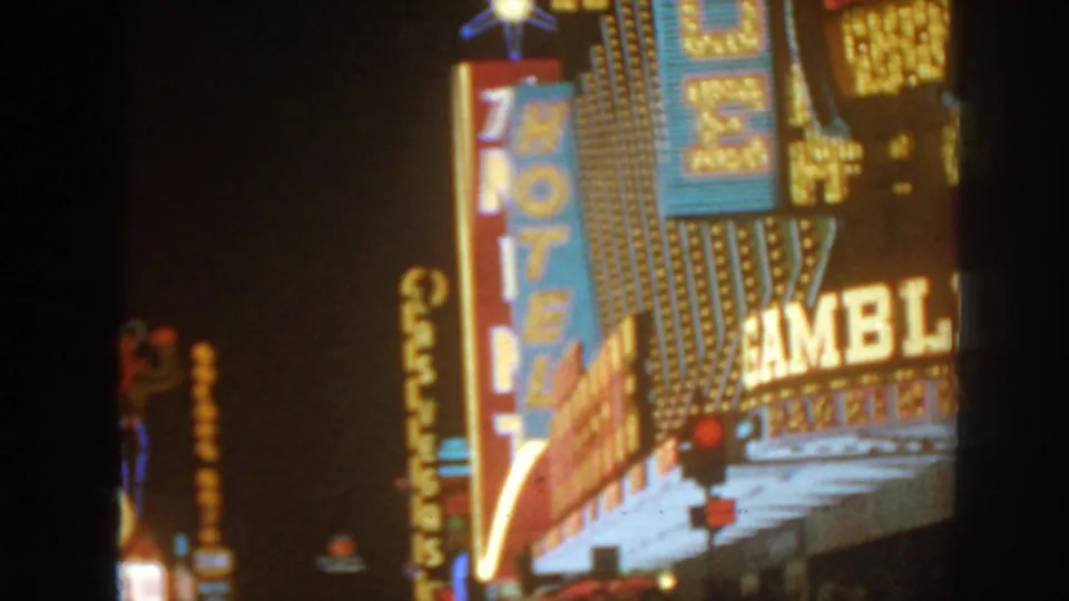 Nighttime 8mm frame of casino gambling signage, vertical neon lettering, and a bulb-lit facade from a visitor viewpoint.