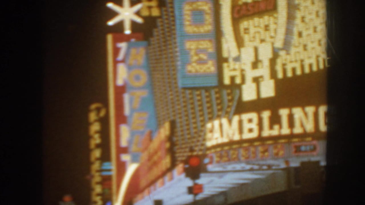 Nighttime illuminated hotel and gambling signage seen from a moving home-movie camera.