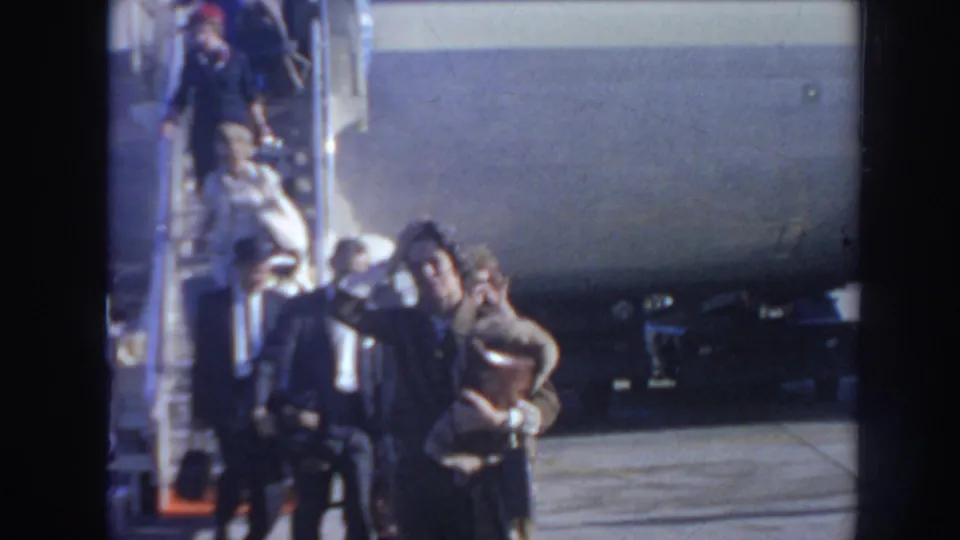 1962 Arizona airport frame with a woman carrying a handbag near other passengers and the side of a Pan Am jetliner.