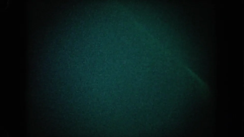 1962 California 8mm frame showing dark blue-green grain, black borders, and a faint curved light trace near the lower center.