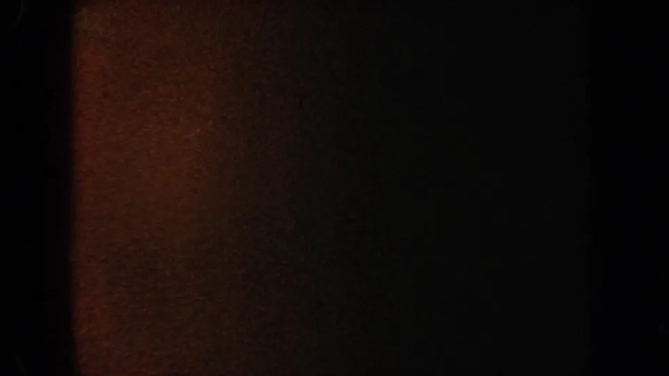 Nearly dark 8mm frame from the aquarium clip, showing reddish-brown exposure, deep shadow, and faint residual tank detail.
