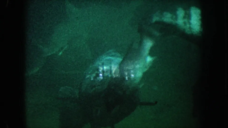 1962 California 8mm frame with a dark fish silhouette above a pale rock or coral-like form in green aquarium water.