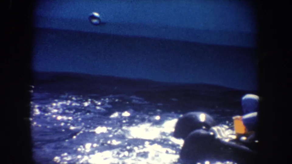 1962 California home-movie frame with sparkling water, distant low hills, and partial people seated near the lower right edge.