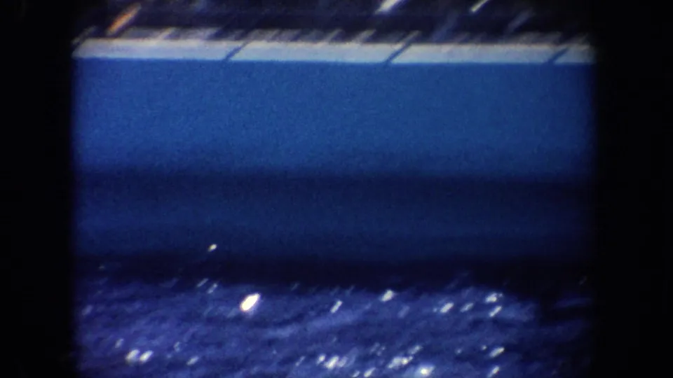 1962 California 8mm frame showing the pool wall, dark water, and a partial striped rail at the edge of the marine show area.