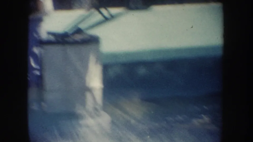Soft 8mm frame from the California water-resort show, with a blurred white platform at the pool edge and blue water beyond.