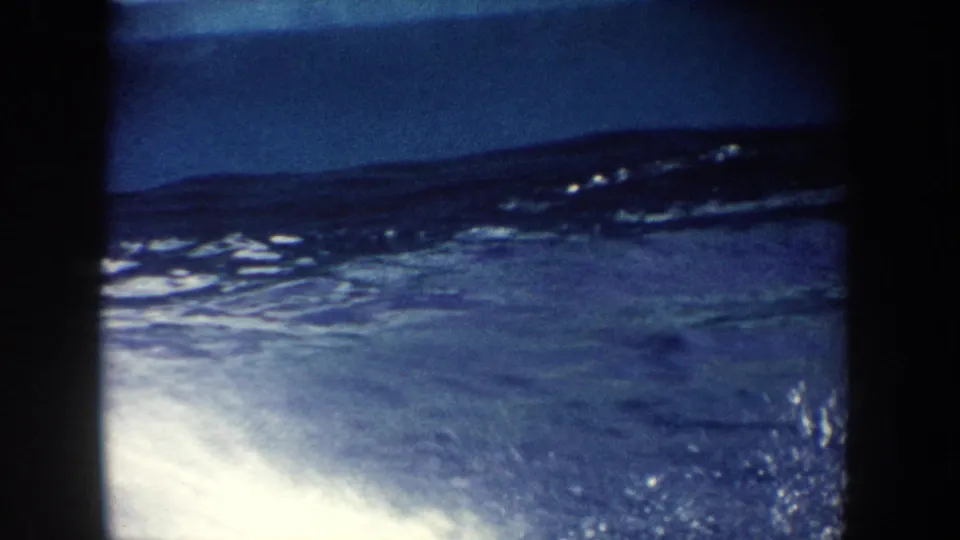 1962 California 8mm frame showing a dolphin partly above the blue pool surface with splashing water during a resort performance.