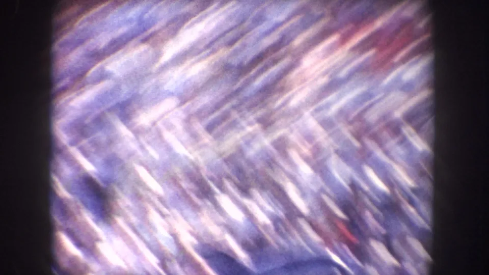 Motion-blurred 8mm frame from the California clip with bright diagonal streaks and indistinct crowd-like color patches.
