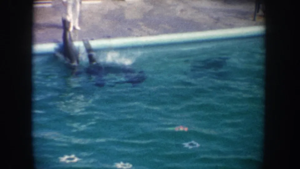 1962 California 8mm frame of a sea lion lifting from the pool near a standing poolside figure and splashing water.