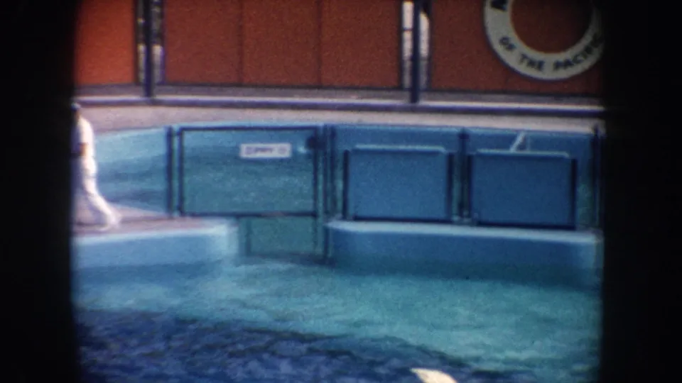A 1962 California marine park view shows the uniformed man partly hidden by the film frame border near the pool and wall signage.