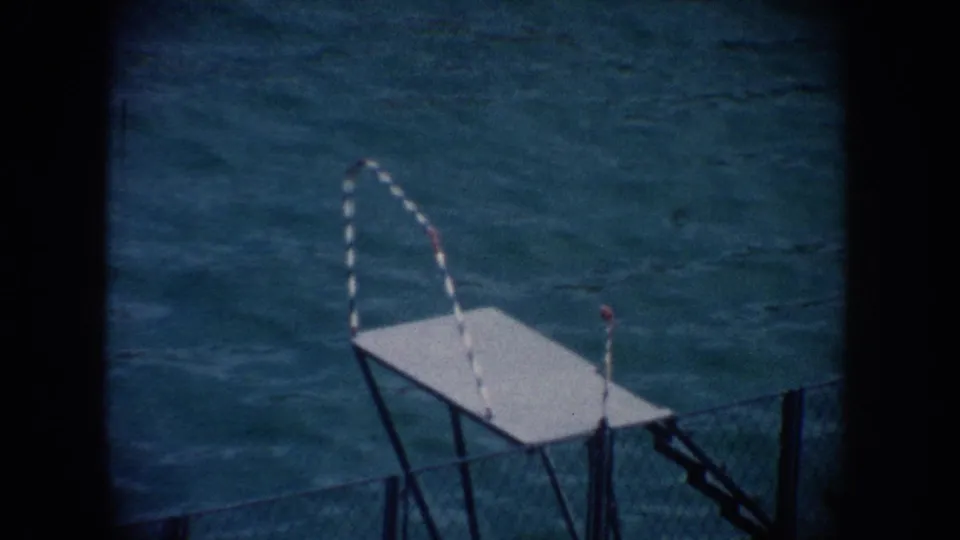 1962 California 8mm frame showing blue pool water, a white platform, and the yellow float near the upper edge of the pool scene.
