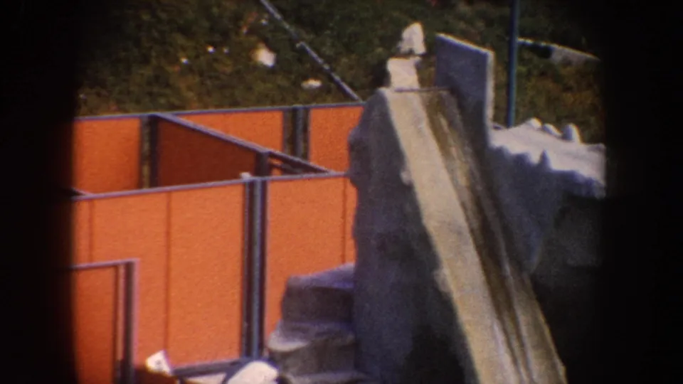A rocky slide-like structure stands beside orange panels and railings in the 1962 California animal exhibit footage.