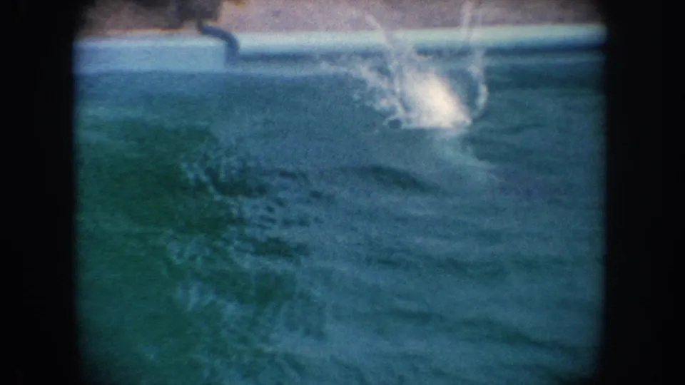 A large splash spreads across turquoise pool water after the seal dives in the 1962 California home-movie footage.
