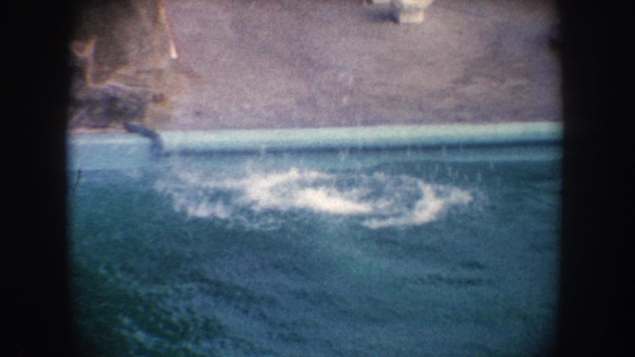 1962 California 8mm frame showing a seal splashing into a zoo pool beside concrete edging and dark film-frame borders.
