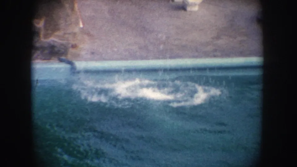 1962 California 8mm frame showing a seal splashing into a zoo pool beside concrete edging and dark film-frame borders.