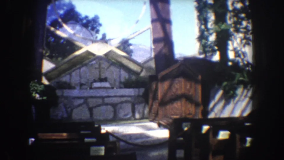 1962 California 8mm frame showing a geometric archway looking toward a stone altar wall with a cross and trees beyond.