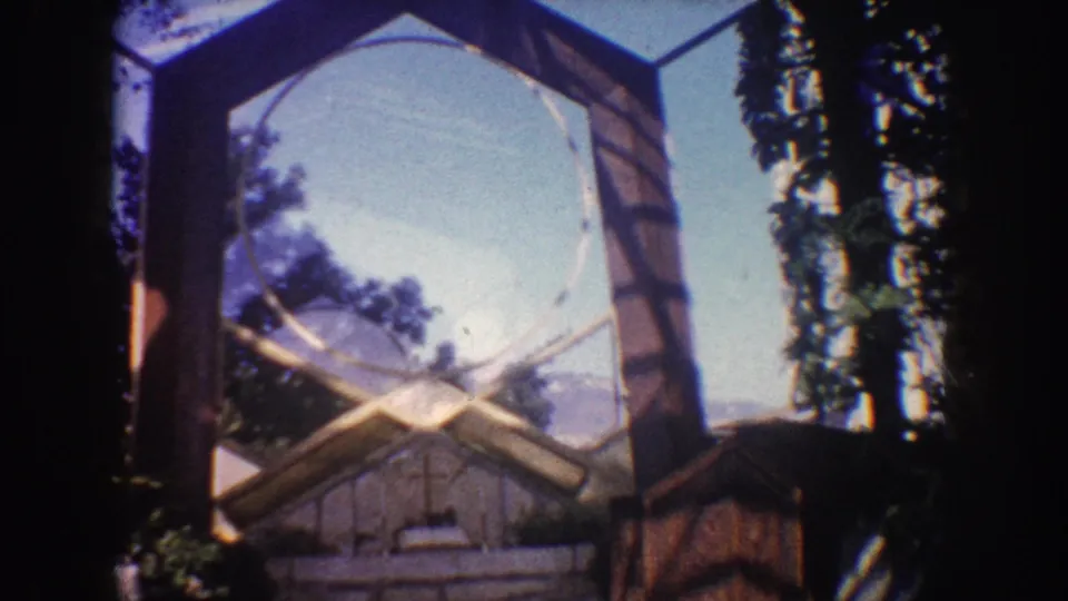 1962 California 8mm frame showing the arch and stone altar area from a visitor perspective, with trees and sky behind it.