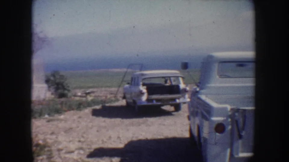 1962 California home-movie frame showing a white station wagon and light-colored pickup truck parked near fields and trees.