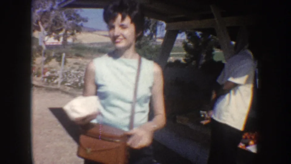 1962 California home-movie frame of a woman near a roadside produce stand during a travel stop.