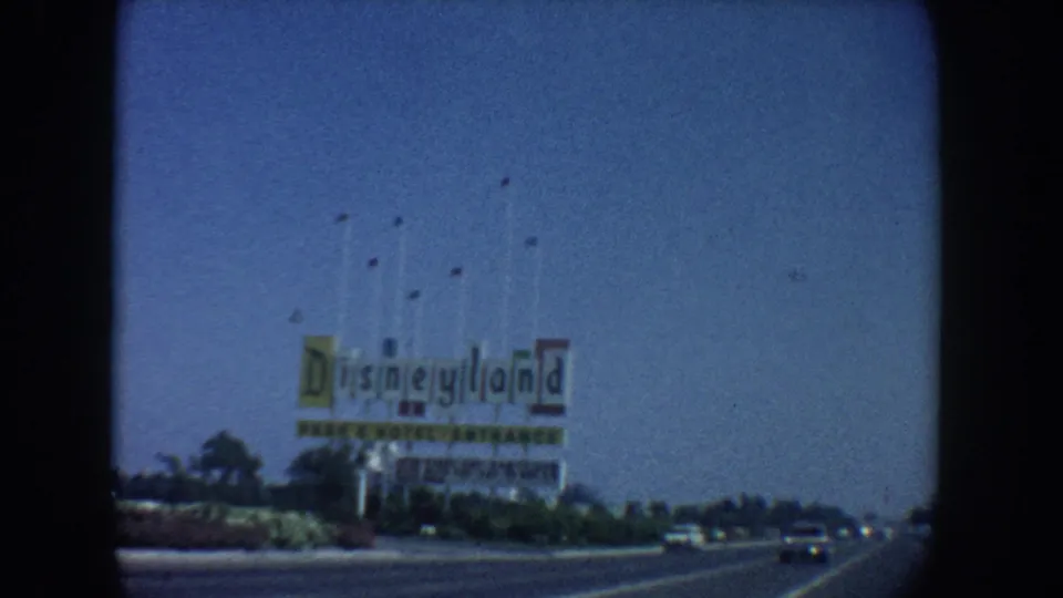 1962 California home-movie view of the Disneyland sign from the road, with cars passing below.