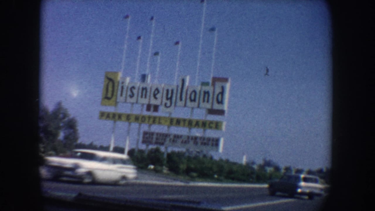 Disneyland entrance sign beside a road with a white car passing in front.