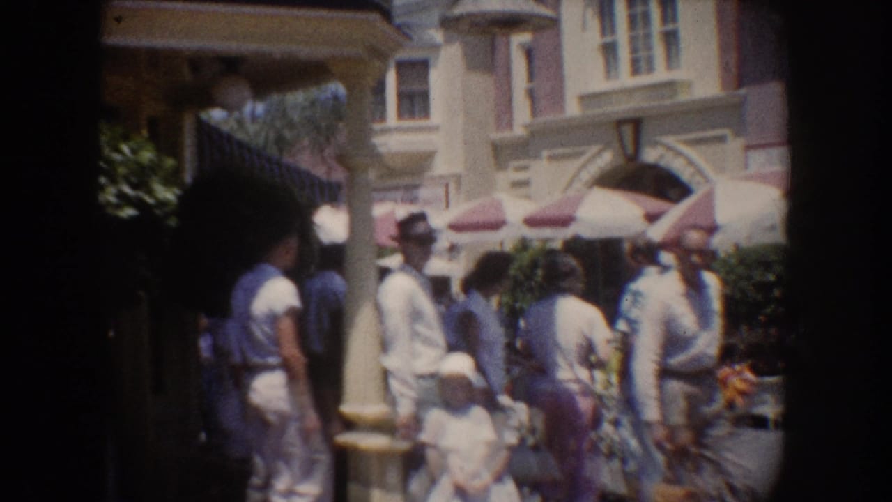 1962 Anaheim street scene with people in hats and light clothing gathered near awnings and decorative storefronts.