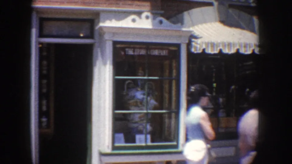 Anaheim storefront facade with a display window, striped awnings, and pedestrians moving through the 1962 street scene.