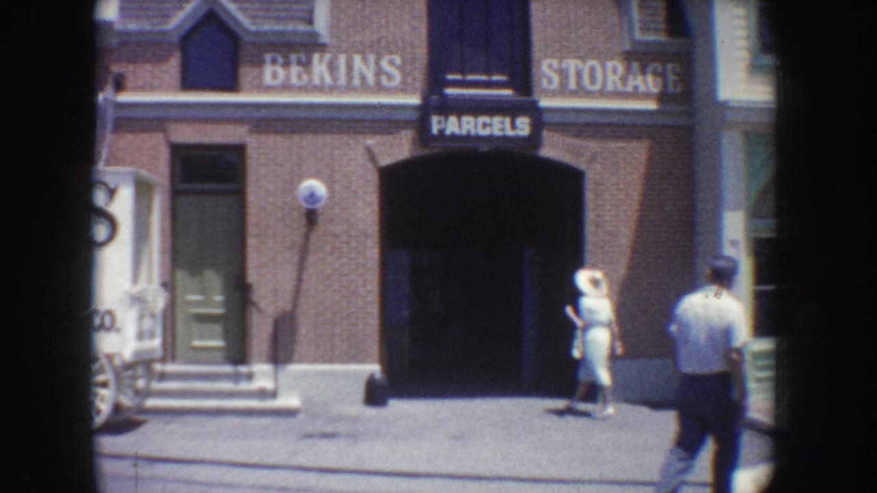 1962 Anaheim street view showing a brick Bekins storage building, sidewalk pedestrians, and a woman in a light dress near the entrance.