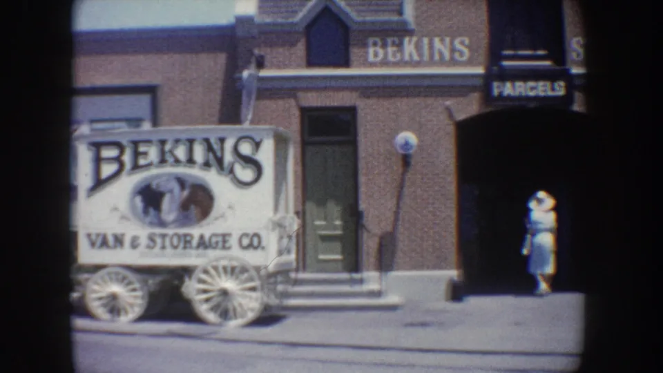 A white Bekins Van and Storage Co. wagon sign sits beside the brick building as a woman walks near the entrance.