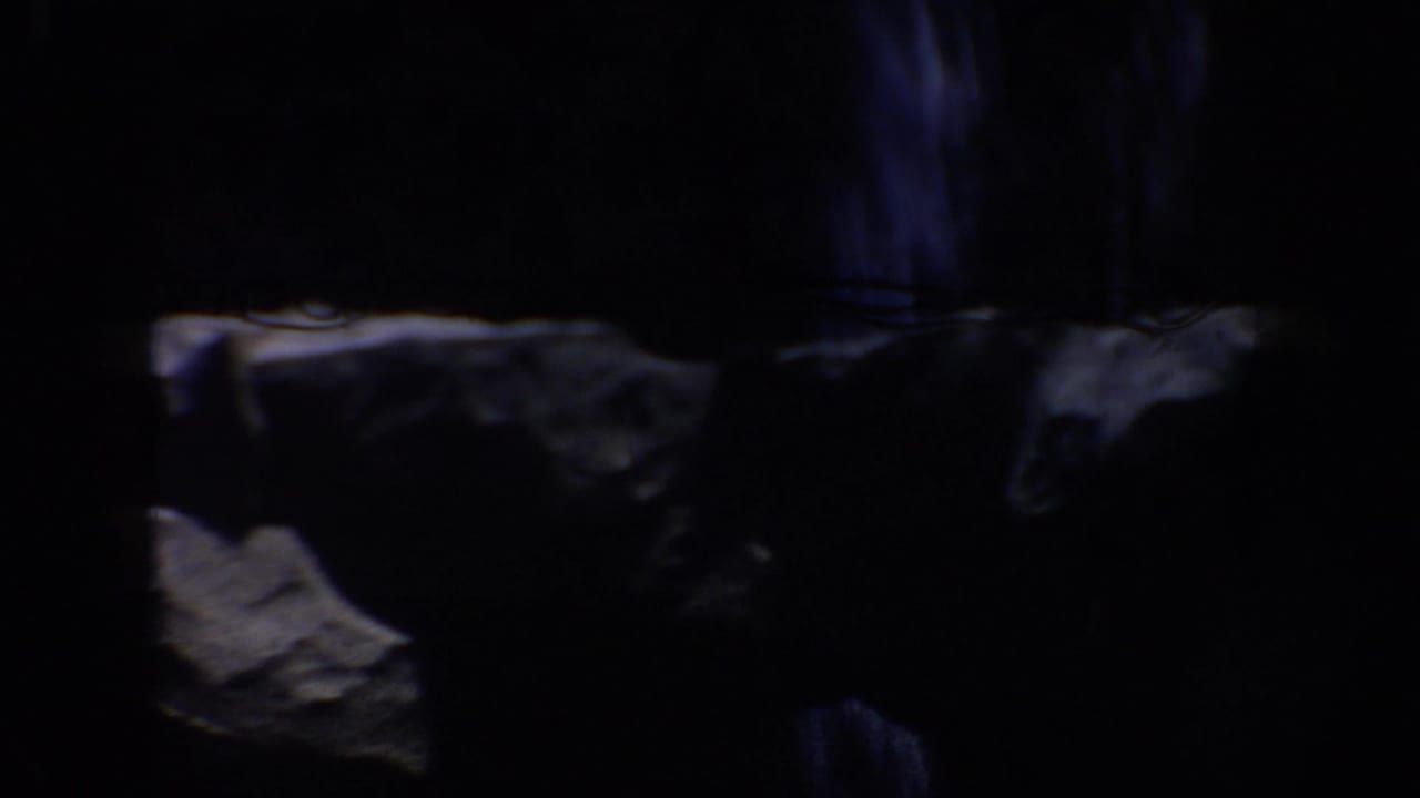 1962 Anaheim home-movie frame showing shadowed artificial rockwork around an amusement ride setting.
